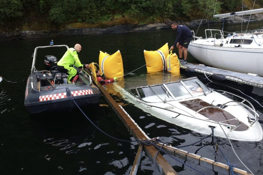 Mannskap fester gule løftesekker til en båt som ligger lavt i vannet ved en flytebrygge